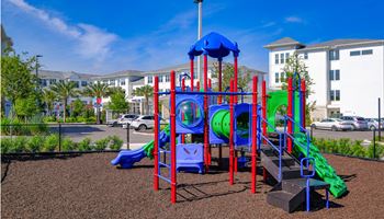 A playground with a blue and red play set in front of a building